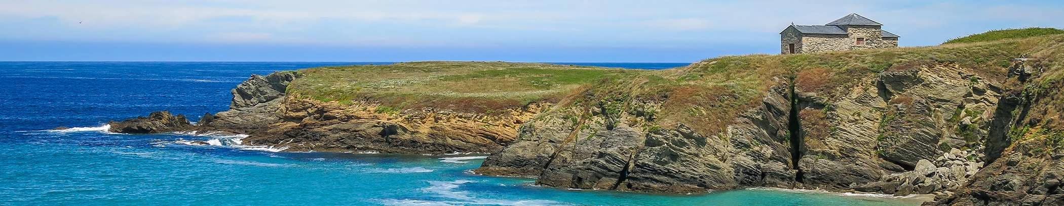 coastal cliffs overlooking the sea on the camino inglés with a small chapel beside the shoreline