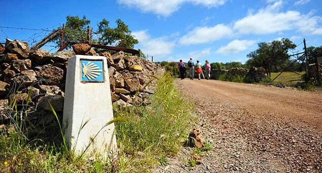 mojón con la concha del camino de santiago junto a peregrinos caminando por un camino rural